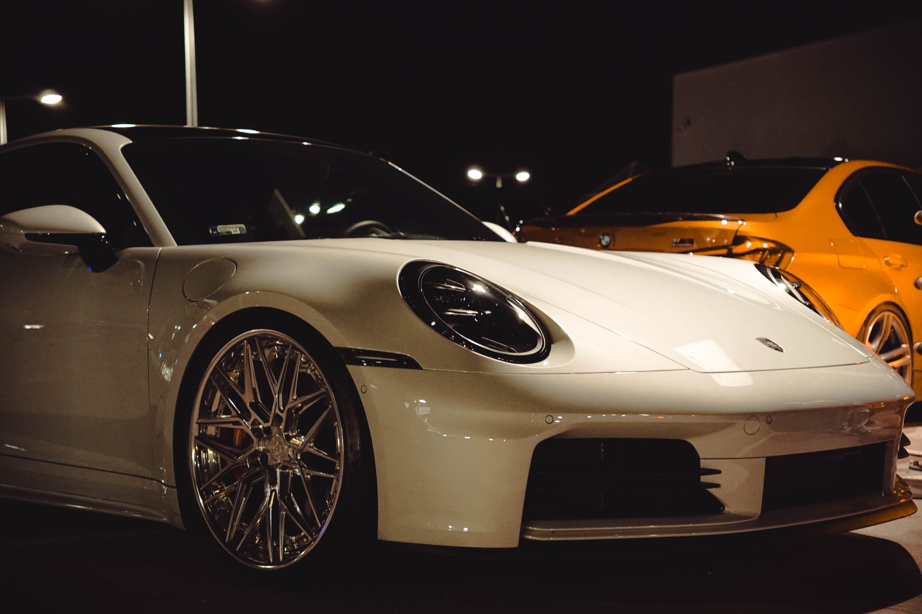 White Porsche 911 next to a yellow BMW at night